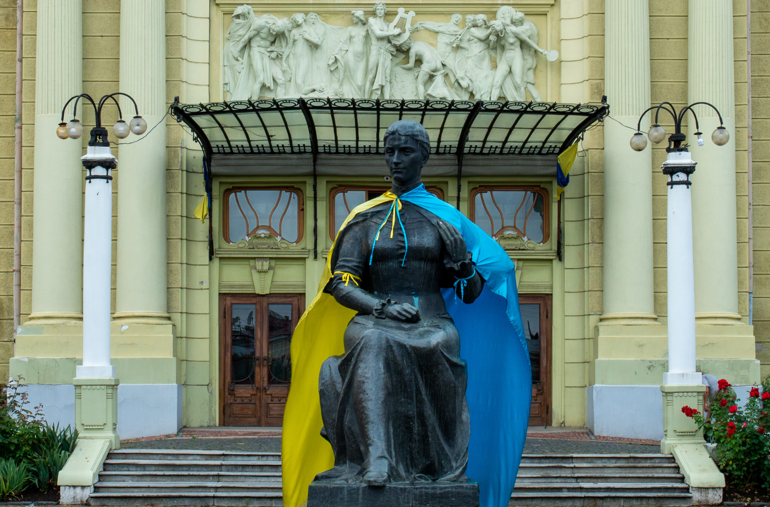Frontalaufnahme einer Bronze von Olga Kobyljanska vor dem Theater Czernowitz, der eine ukrainische Flagge umgebunden wurde.
